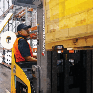 Man in warehouse using machinery to handle inventory, representing the inventory carrying costs involved in warehousing