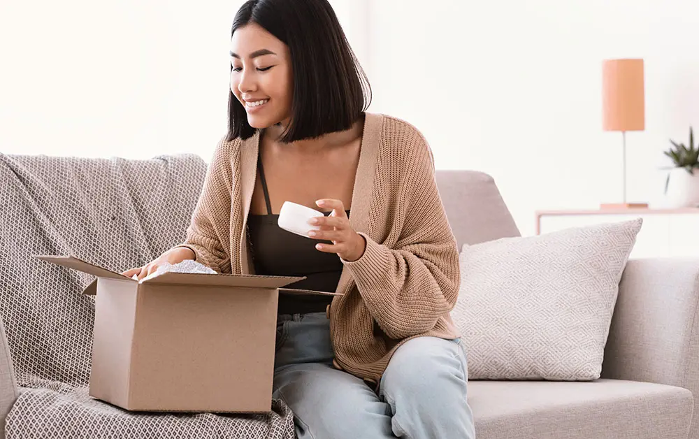 Smiling woman unpacking cardboard beauty box with cosmetics product
