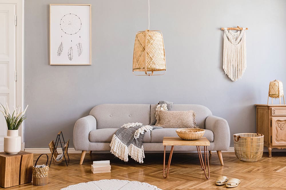 Stylish and design home interior of living room with gray sofa, wooden cube, commode, pillow, macrame, rattan lamp, basket, plants and elegant accessories.